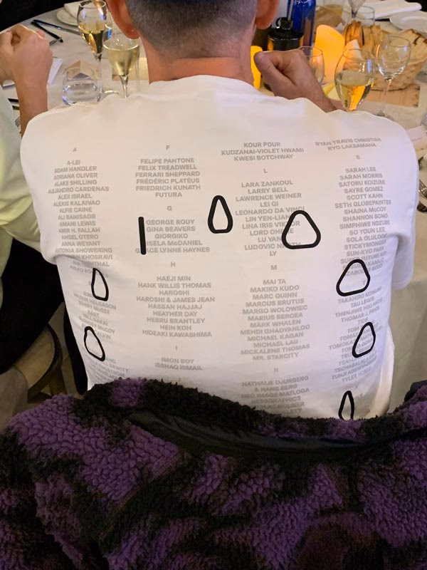 Person wearing a white shirt with grey text and black shapes at a table