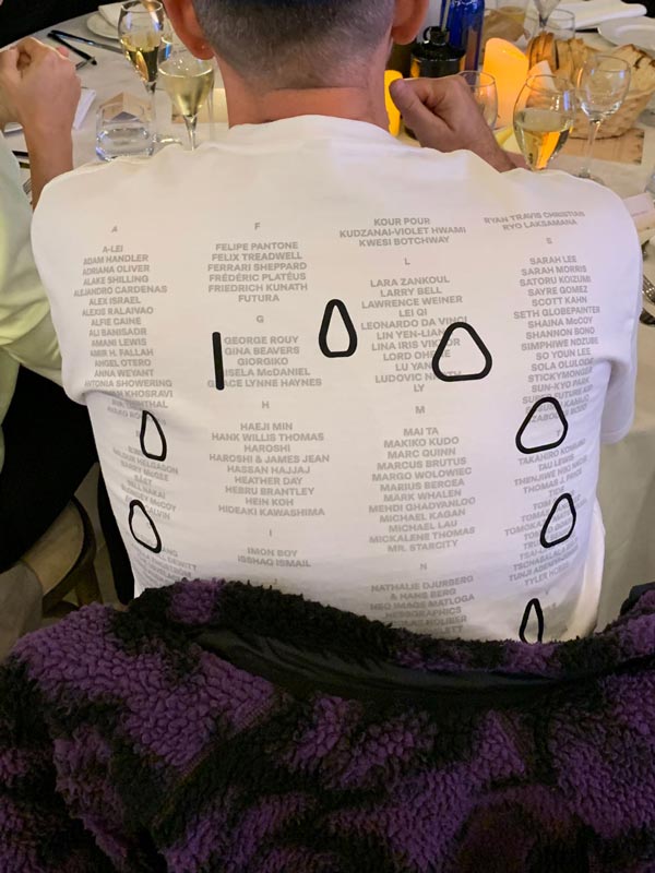 Person wearing a white shirt with grey text and black shapes at a table