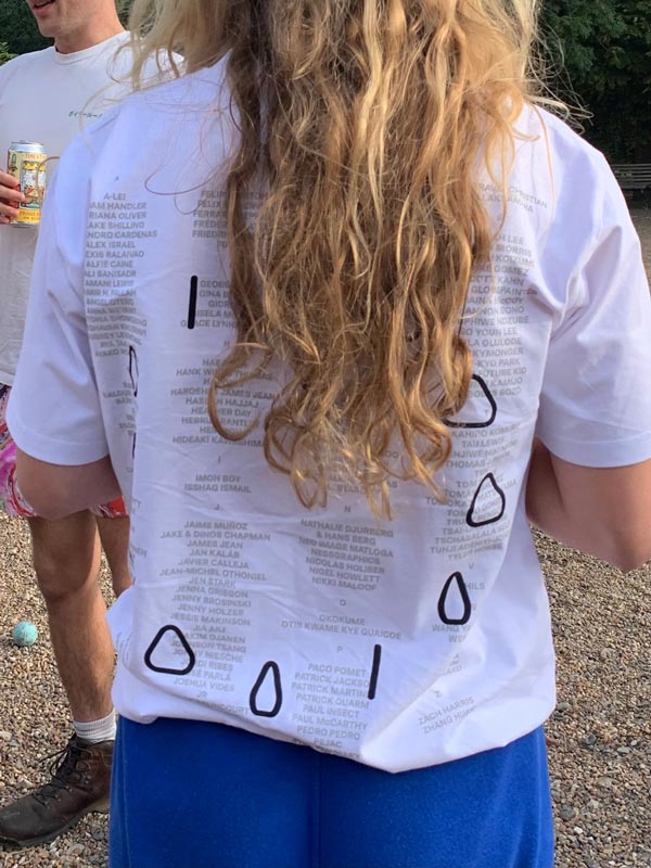 Person with long hair wearing a white shirt with grey text and black shapes