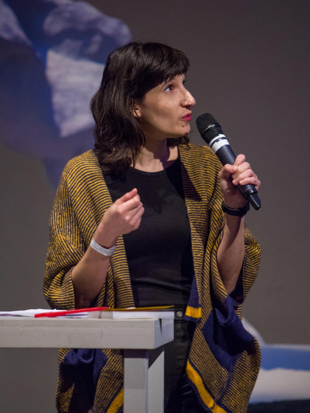 Woman speaking into a microphone with some of the set design pieces in the background